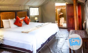 Bedroom interior, the bed has white linen, canvas tent side and the bathroom in the background