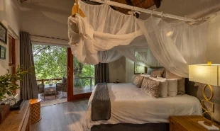 Bedroom with King bed, light colors, mosquito net and glass doors in the back ground
